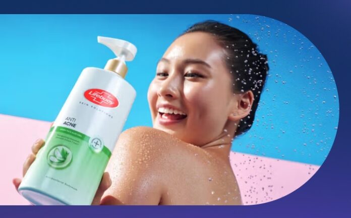 A smiling woman holds Lifebuoy Anti Acne antibacterial body wash -– a white and green bottle with a red Lifebuoy logo.